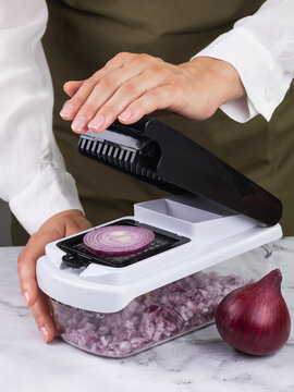 Woman dicing red onion with handheld vegetable chopper slicer on marble table close-up