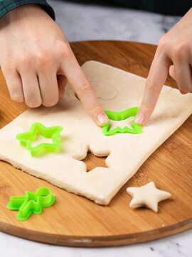 Child's hands cutting shapes with green cookie cutters from rolled dough on wooden board for baking cookies close-up