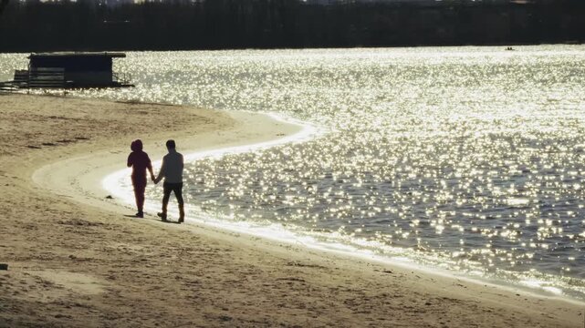 Couple Holding Hands Walking Along Sandy Beach. Romantic Lovers Strolling Near Sparkling Water