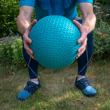 male wearing compression sleeves is exercising with a heavy slam ball, functional fitness and backyard gym concept