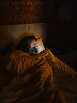 Woman lying awake in bed with smartphone 