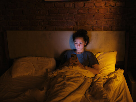 Woman lying awake in bed with smartphone 