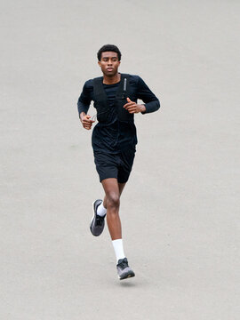 Man Runs on a Concrete Path in Black Sportswear and Shoes