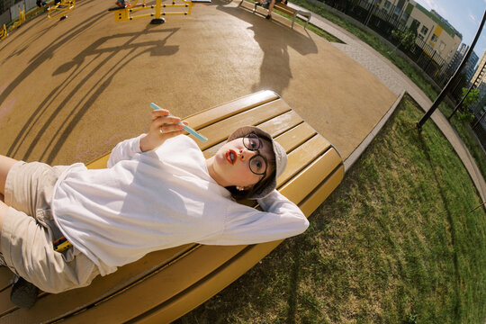 Young Person Relaxes on Bench While Using Mobile Phone at Outdoor Gym