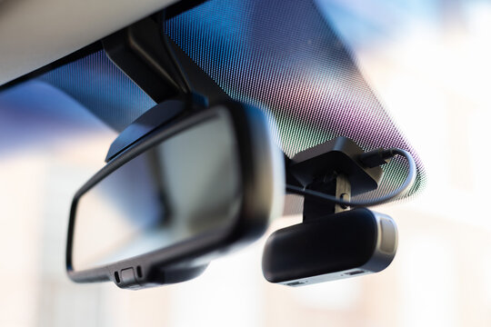 Closeup windshield frit pattern with mounted dash camera beside mirror bracket, cool blue purple reflections, cabin hardware, glass texture, and soft light, with windshield, frit, dotmatrix, dashcam