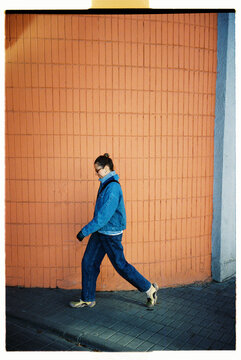 Woman walks along a brick wall while wearing a blue jacket