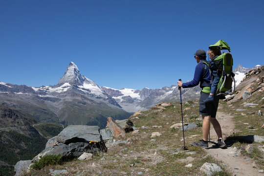 father hikes with child in carrier backpack, Zermatt, Switzerland
