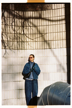 Woman stands against a wall wearing sunglasses and a jacket