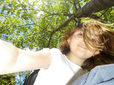 Child Looking Down at Camera Beneath Tree Canopy on Sunny Day