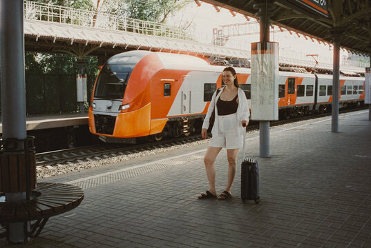 A woman laughs on a sun-warmed train platform with her luggage