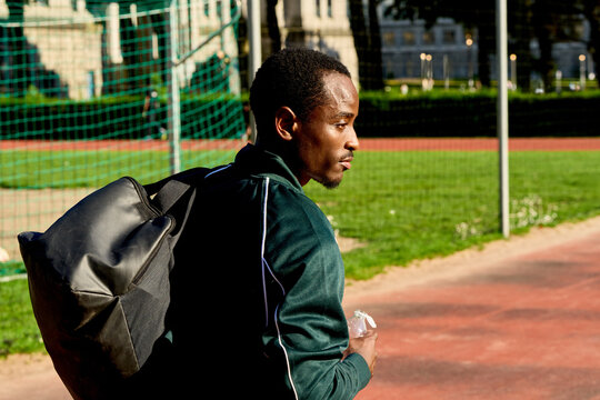 Man Walks With Bag on Track at Sports Field Near Buildings