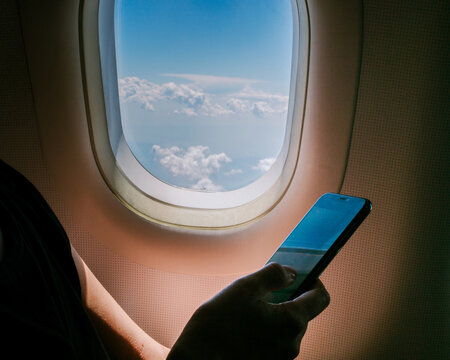 Person Looks at Phone by Airplane Window During Flight