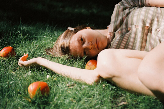 A young woman with freckles smiles softly in dappled sunlight