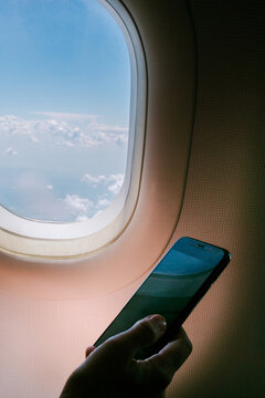 Person Looks at Phone by Airplane Window During Flight
