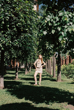 A woman stands between rows of trees in a city park