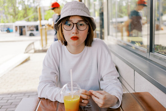 Young Woman Sits at Table With Drink in Outdoor Setting