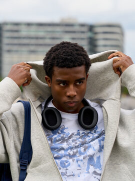 Young Man Adjusting Hoodie in Urban Setting With Headphones On