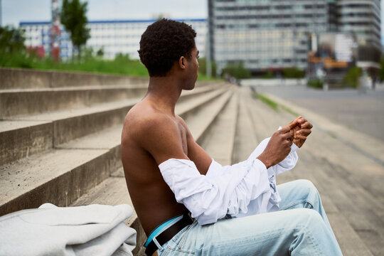 Young Man Sits on Steps in City and Looks Away at Buildings
