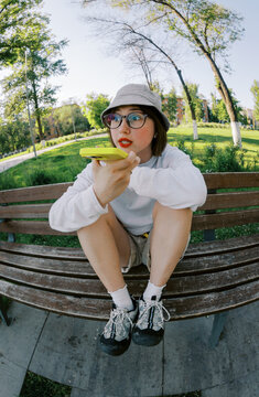 Woman Sitting on Bench Speaking Into Phone in a Park