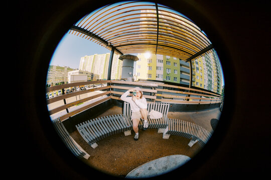 Person Sitting with camera on Bench Under Wooden Shelter in Urban Area