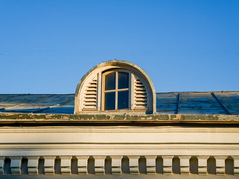 Semicircular dormer window with wooden ventilation louvers on the roof of an old historical building