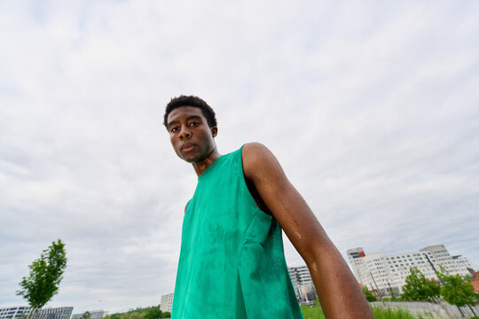 Model Poses in Green Outfit Under Cloudy Sky in Urban Setting