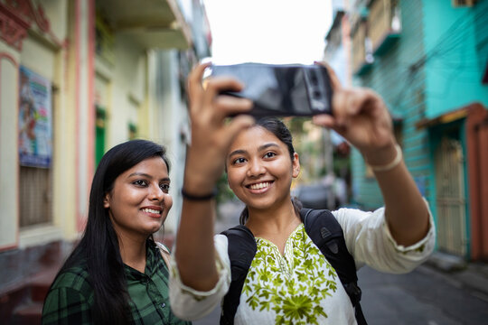 Two young girl taking selfie shots in the street of a city 