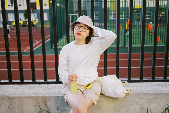 Young Person Relaxes With Drink Near Sports Field in Warm Weather