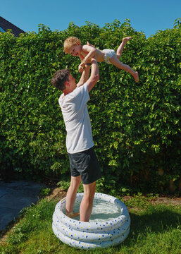 Parent Lifts Child Above Small Pool in Sunny Backyard