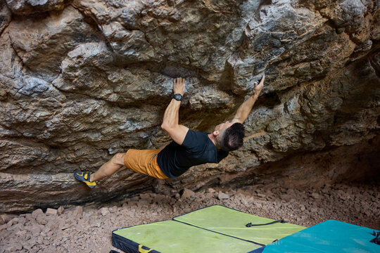Climber reaches for hold on rock wall in outdoor bouldering spot