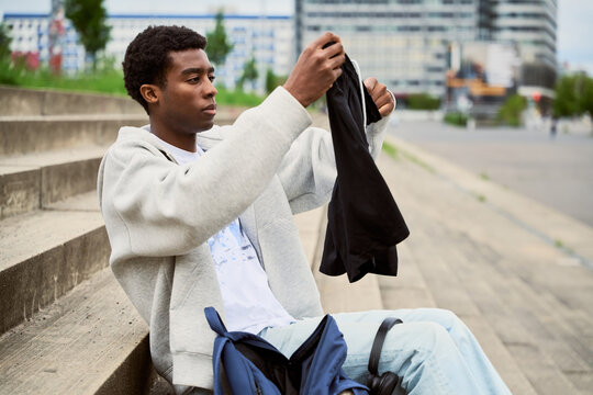 Young Man Looks at Black Shirt While Seated on Outdoor Steps
