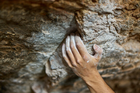 Climber grips rocky surface while bouldering indoors at gym