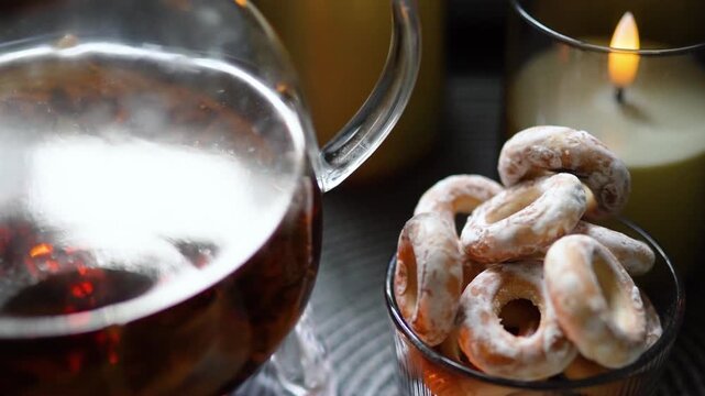 Cozy evening tea served in a glass teapot with fresh bagels and cookies on a rustic table. Warm candlelight creates a relaxing, homely atmosphere perfect for autumn or winter evenings