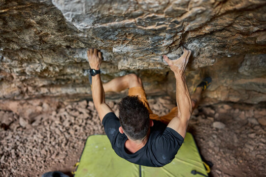 Climber uses handholds to ascend rock wall in outdoor setting