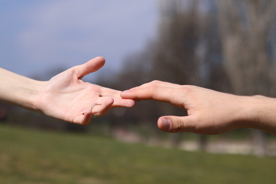 Close up of two hands reaching out to each other against a blurred park background, connection and relationship concept