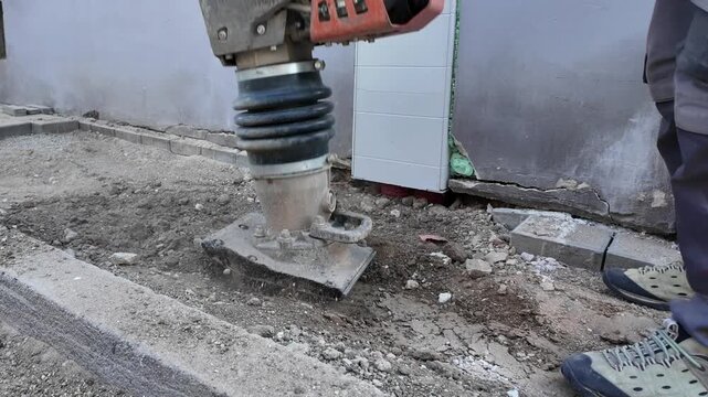 Construction worker compacting soil with a plate compactor near a building wall