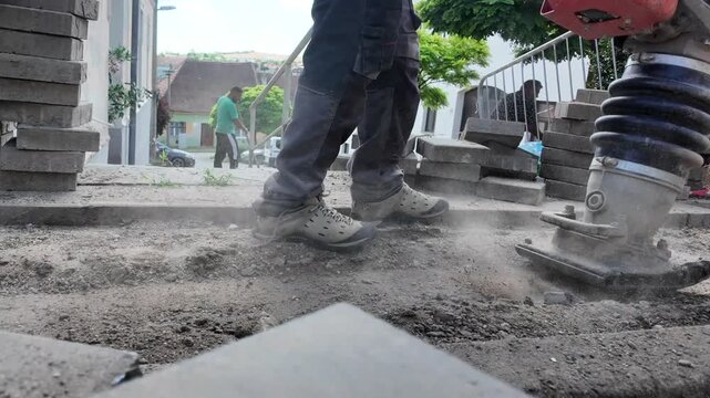 Construction workers compacting ground with vibratory tamper for paving project