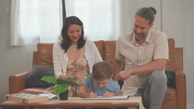 Loving parents watching their little boy draw and colour with crayons and paper