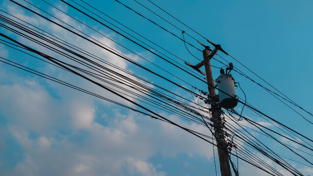 Electricity transmission utility pole featuring a detailed electrical transformer connected to a complex web of overhead power lines against a clear blue sky