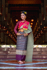 Fototapeta premium Thai woman in elegant traditional Royal Chakraphat dress and golden jewelry holding folding fan, posing inside ancient temple vihara