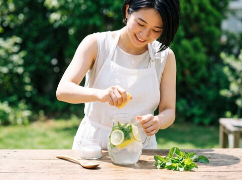 Woman squeezing fresh lemon into homemade infused water with mint and ice