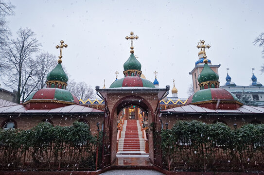 Snowflakes falls gently over an Orthodox monastery, dusting its domes and golden crosses in white snow, while festive lights twinkle in the twilight. Serene winter scene capturing the spiritual beauty