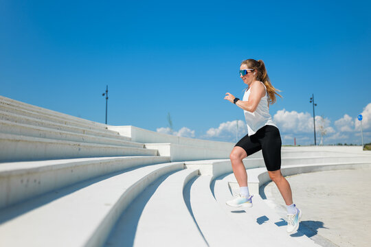Woman exercising on outdoor steps under a bright blue sky on a sunny day while wearing stylish athletic gear