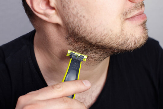 Close-up of a young man trimming his beard and stubble on the neck with a modern electric trimmer