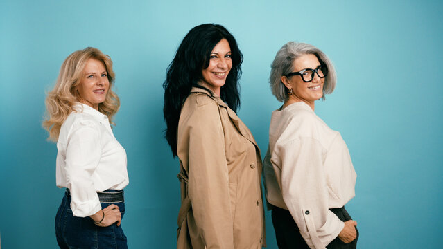 Three generations of women smiling, standing side by side against a blue background, embracing friendship and togetherness