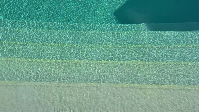 Sunlit pool steps leading into crystal clear turquoise water with sparkling reflections, inviting beginning of a luxury vacation, resort lifestyle, summer relaxation, wellness retreat, peaceful escape
