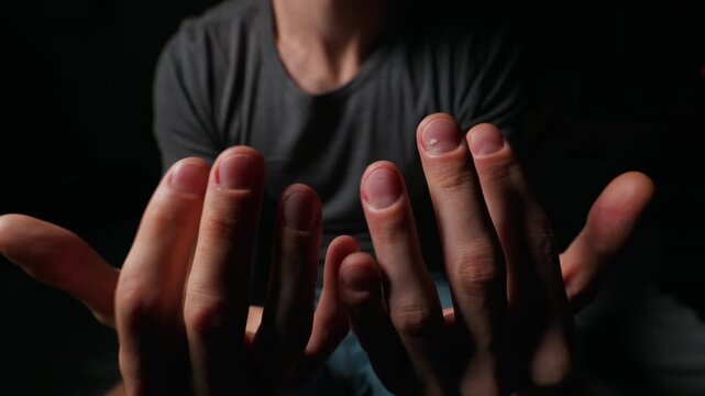 A man holds out his hands and showcases his fingernails and cuticles under dramatic lighting. Concept of skin care, nail health, calcium deficiency, male grooming, and body awareness.
