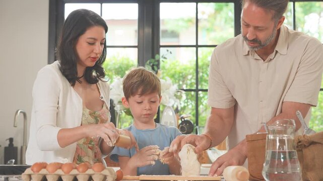 Little boy learning to bake bread with his mum and dad at the kitchen worktop