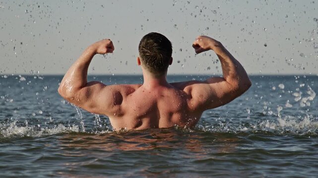 Physique back shows wet muscles. Physique pose looks strong outdoors. Athletic physique concept shows wellness. Shirtless physique shows body power.