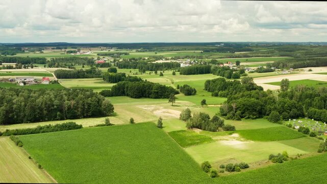 Green agricultural fields expand across a flat European plain. This rural landscape shows sustainable agriculture development, diverse crop farming patches, and small countryside villages.